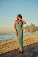 High-fashion shot of a model in the Menita navy cotton maxi dress standing on a beach boardwalk at sunset.
