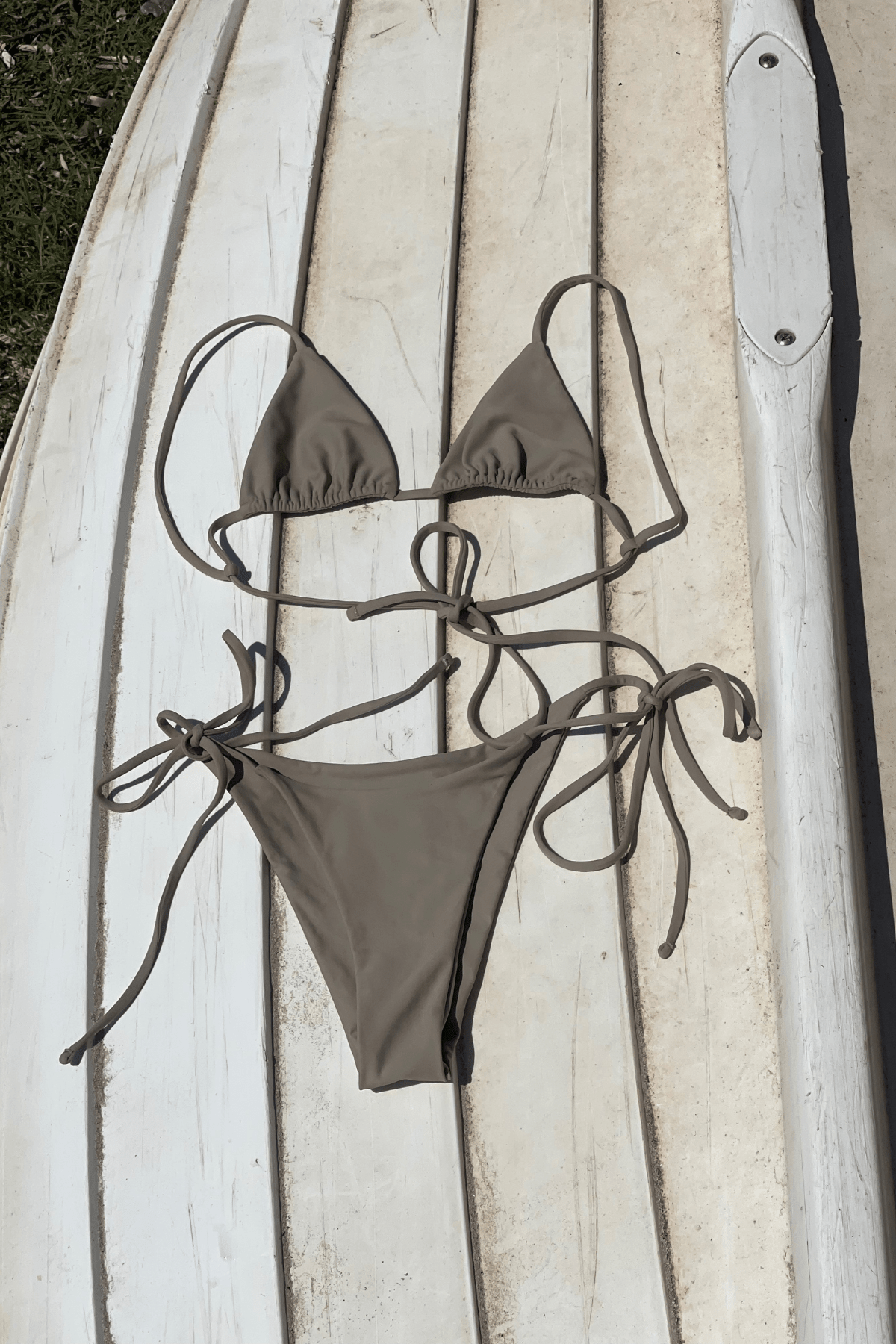 Brown bikini set on a wooden surface with a surfboard in the background
