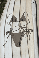 Brown bikini set on a wooden surface with a surfboard in the background