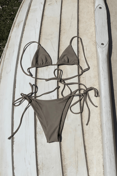 Brown bikini set on a wooden surface with a surfboard in the background